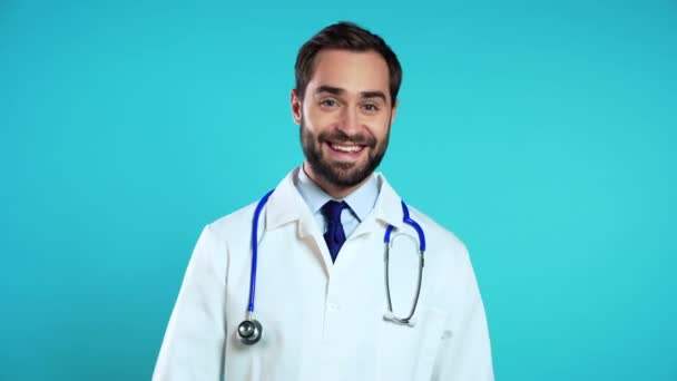 Ritratto di medico positivo sorridente in mantello bianco medico professionale che mostra i pollici verso l'alto gesto. Doc isolato su sfondo blu . — Video Stock