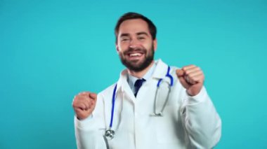 Profesyonel beyaz önlüklü yakışıklı doktor mavi stüdyo arka planında izole edilmiş. Sakallı doktor. Komik dans, başarı ve işte şans..