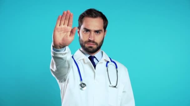 Retrato de médico serio en bata blanca médica profesional que muestra gesto de rechazo por señal de stop palm. Doc hombre aislado sobre fondo azul. — Vídeos de Stock