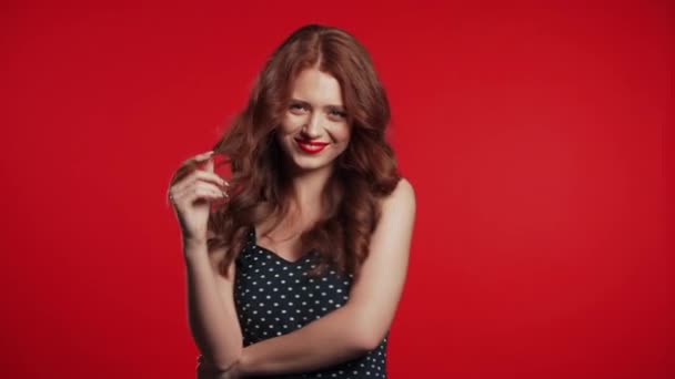 Ładna młoda dziewczyna z rudymi włosami stojąca na tle studia, uśmiechnięta i flirtująca. Ładny portret kobiety z czerwonymi ustami — Wideo stockowe