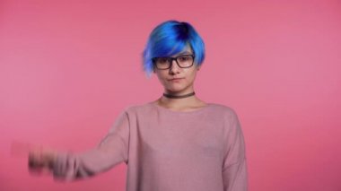 Young unusual woman with blue hair making disapproving with no finger sign, negation gesture over pink studio background