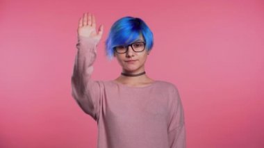 Young unusual girl with blue hair making stop palm gesture over pink studio background. No, never, woman disliking and rejecting