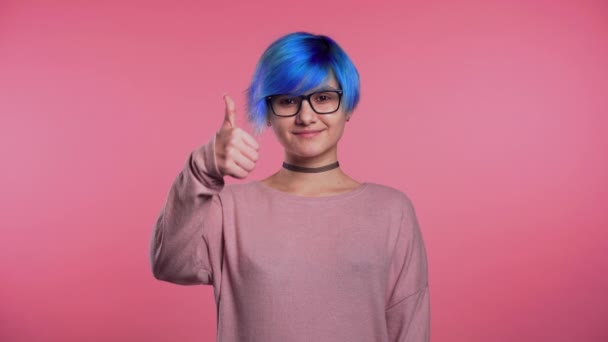 Jovem punk mulher incomum com cabelo azul fazendo polegares para cima sinal sobre fundo rosa e sorrisos para a câmera . — Vídeo de Stock