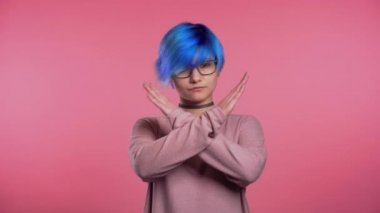 Young unusual woman with blue hair making no crossing hands sign, negation gesture over pink studio background 