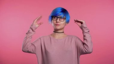 Cute woman with blue hair showing bla-bla-bla gesture with hands and rolling eyes isolated on pink background. Empty promises, blah concept. Lier.