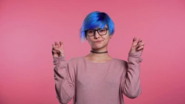 Mavi saçlı, elleri tırnak işareti gibi iki parmağı olan güzel bir punk kızı pembe arka planda izole edilmiş parmaklarını bük. Çok komik, ironi ve alaycılık konsepti..