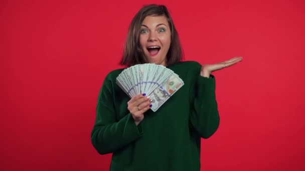 Glad upphetsad flicka i grön tröja visar pengar - amerikanska dollar sedlar valuta på röd vägg. Symbol för framgång, vinst, seger. — Stockvideo