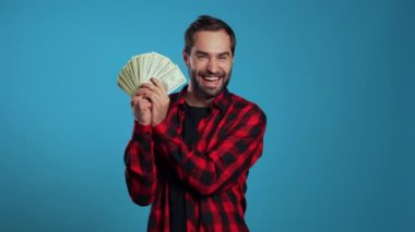 Mutlu ve mutlu bir adam mavi duvarda Amerikan doları banknotları gösteriyor. Başarı, kazanç, zafer sembolü.