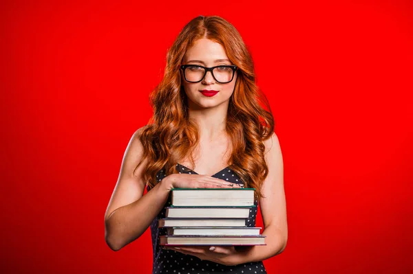 Serious female student on red background in studio holds stack of university books from library. Woman in glasses. — 스톡 사진