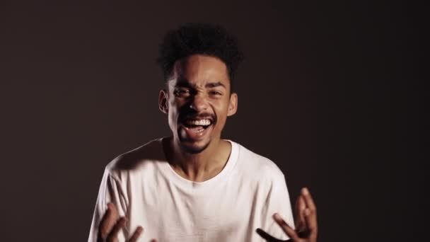 Young african stressed man in white shirt shouting isolated over dark background. Angry and depressed guy loudly screaming to camera. — 비디오