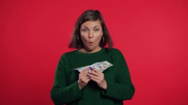 Yeşil kazaklı mutlu kız kırmızı duvarda Amerikan doları banknotları gösteriyor. Başarı, kazanç, zafer sembolü.