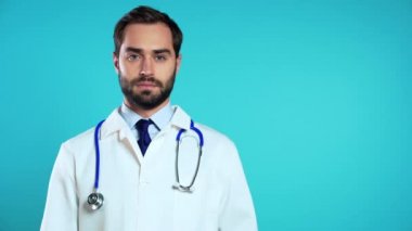 Profesyonel medikal beyaz önlüklü genç adamın uzay portresi mavi stüdyo arka planında izole edilmiştir. Sakallı ve steteskoplu doktor.