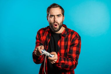 Mavi stüdyo duvarında joystick ile TV 'de video oyunu oynayan yakışıklı genç adam. Modern teknolojiyi kullanarak.