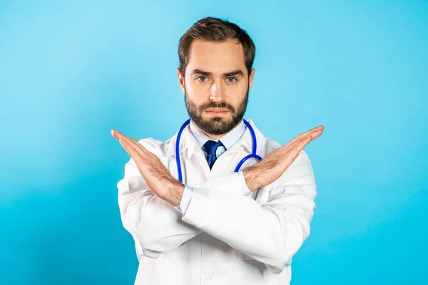 Portret poważnego lekarza w profesjonalnym medycznym białym płaszczu bez znaku krzyżowania rąk wykonać gest negacji. Zaprzeczanie, odrzucanie, niezgoda. Doc Man odizolowany na niebieskim tle. — Zdjęcie stockowe