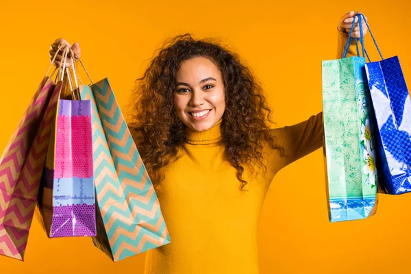 Glückliche junge Frau mit bunten Papiertüten nach dem Einkauf isoliert auf gelbem Studiohintergrund. Saisonverkauf, Einkäufe, Ausgaben für Geschenkideen — Stockfoto