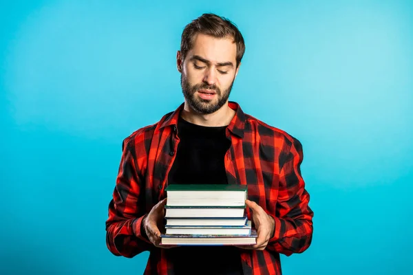 European student on blue background is dissatisfied with amount of homework and books. Man confused, he is annoyed, discouraged frustrated by studies.