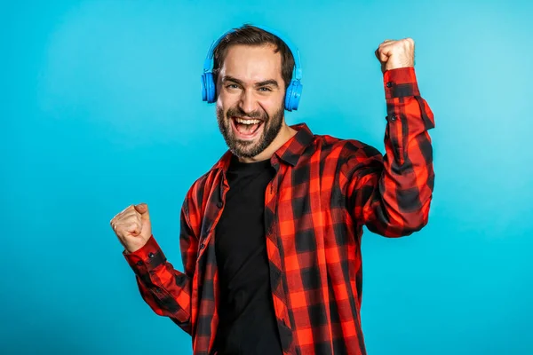 Un bel homme avec des écouteurs dansant isolés sur fond bleu. Fête, musique, style de vie, concept radio et discothèque . — Photo