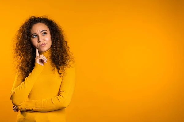 Thinking woman looking up and around on yellow background. Worried contemplative face expressions. Pretty curly girl model — 스톡 사진