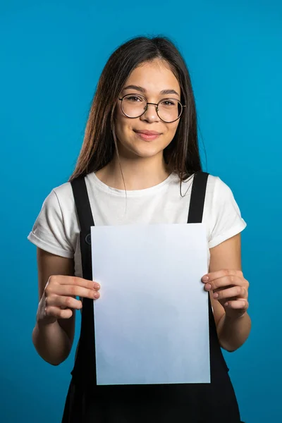 Muito asiático menina segurando branco a4 papel cartaz. Espaço para cópia. Sorrindo mulher da moda com cabelos longos no fundo do estúdio . — Fotografia de Stock