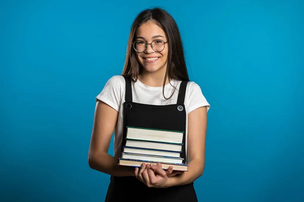 Asian student girl on blue background in the studio holds stack of university books from library. Woman smiles, she is happy to graduate. — Stock Photo, Image