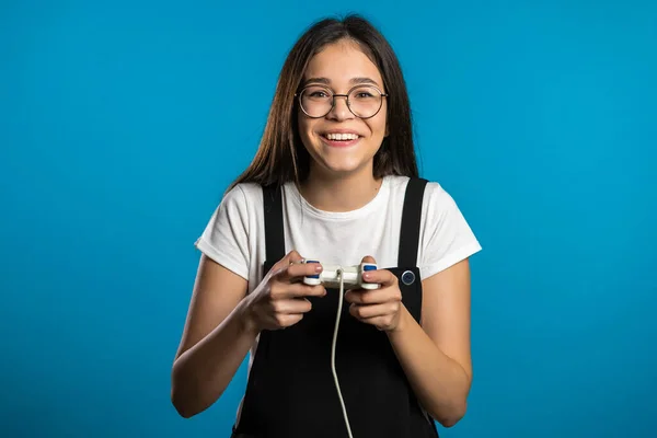 Mooi Aziatisch meisje spelen video spannend spel op TV met joystick op blauwe studio muur. Gebruik van moderne technologie. — Stockfoto