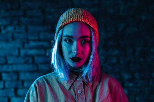 Jeune femme en néon rose et bleu. Portrait de belle fille punk insolite avec coiffure colorée sur fond de studio mur de briques — Photo
