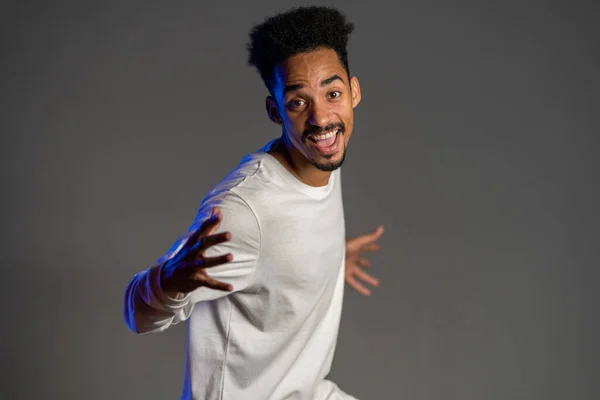 Joven hombre afroamericano muy activo y enérgico en ropa blanca sonriendo y bailando de buen humor sobre fondo gris — Foto de Stock