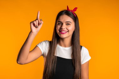 Düşünen genç bir kadının portresi sarı stüdyo arka planında bir fikir yakaladığı an. Gülümseyen mutlu kız, Eureka hareketi yapıyor.