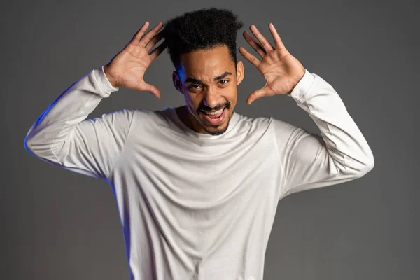 Joven hombre afroamericano muy activo y enérgico en ropa blanca sonriendo y bailando de buen humor sobre fondo gris — Foto de Stock