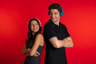 Kırmızı arka planda izole edilmiş kulaklıklarla dans eden genç Amerikalı çift. Parti, mutluluk, müzik konsepti.