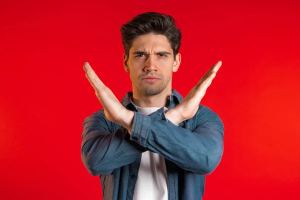 Man disapproving with no crossing hands sign make negation gesture. Denying, Rejecting, Disagree, Portrait of handsome guy on red background — Stock Photo, Image