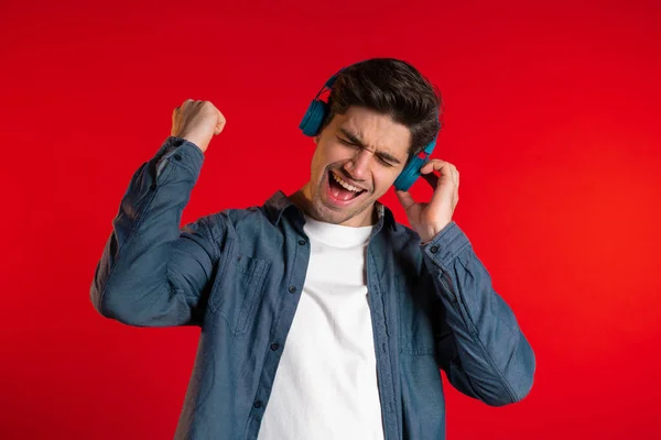 Un bel homme avec des écouteurs dansant isolés sur fond rouge. Fête, musique, style de vie, concept radio et discothèque . — Photo