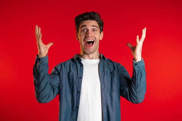 Man in blue shirt very glad and happy, wow effect, he smiling, screaming. Surprised excited happy guy on red studio background — Stock Photo, Image