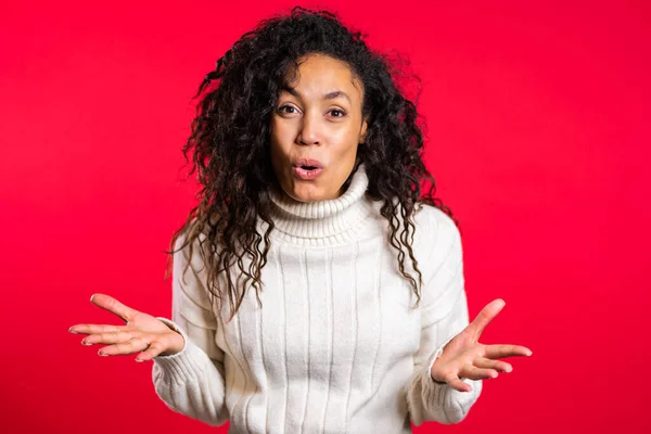 Pretty female shocked model on red background. OMG, wow effect. African girl with long hair with delight. Surprised excited happy woman in sweater — Stock Photo, Image