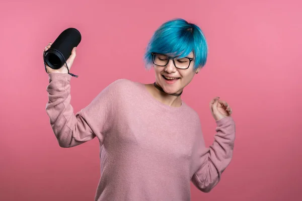 Nette Frau mit blauen Haaren lächelt und tanzt mit drahtlosen tragbaren Lautsprechern im rosa Studiohintergrund. Musik, Tanzkonzept — Stockfoto