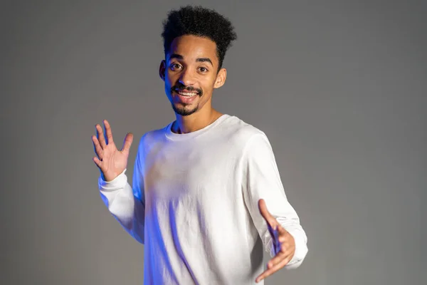 Joven hombre afroamericano muy activo y enérgico en ropa blanca sonriendo y bailando de buen humor sobre fondo gris — Foto de Stock