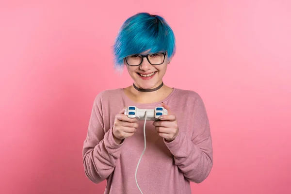 Hübsches junges Mädchen mit blauer Frisur beim Videospiel auf dem Fernseher mit Steuerknüppel an der rosafarbenen Studiowand. Einsatz moderner Technologie. — Stockfoto