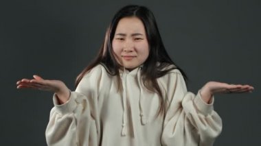 Beyaz kapüşonlu, kendinden emin olmayan genç Asyalı kız kollarını silkiyor, benim bilmediğim, umursamadığım, yardım edemediğim jestler yapıyor. Gri stüdyo geçmişi