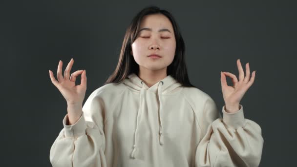 Lugn asiatisk flicka koppla av, meditera. Kvinna lugnar ner sig, andas djupt med mudra om på grå studio bakgrund — Stockvideo