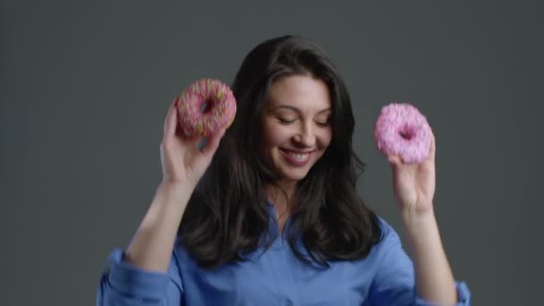 Porträt einer fröhlichen schönen erwachsenen Frau, die mit Bonbons und bunten Donuts auf grauem Studiohintergrund tanzt. Konzept von Freude, Glück, Lebensstil. — Stockvideo