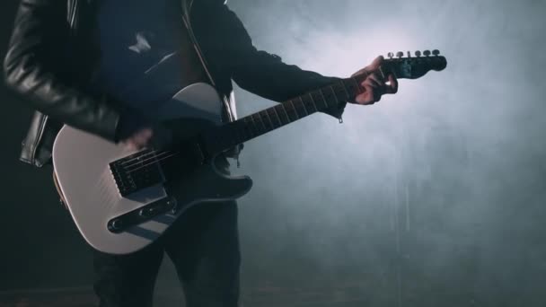 스모키 스튜디오 나 무대에서 록음 악가 가 흰 전기 기타아 를 능숙하게 연주 한다. 어두운 방에서 알아볼 수없는 기타 연주자를 가까이 서 볼 수있다. 느린 동작 4K — 비디오