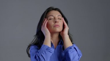 Uzun saçlı, başı ağrıyan, stüdyo portresi olan sıkılmış olgun bir kadın. Kafaya dokunan kız, gri arka planda soyutlanmış. Sorunlar ve baş ağrısı kavramı.