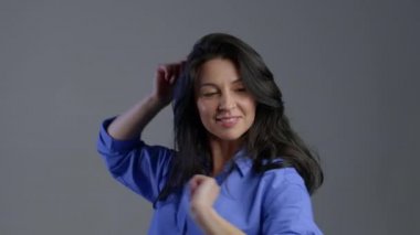Gri stüdyo arka planında izole bir şekilde dans eden neşeli yetişkin kadın portresi. Neşe kavramı, mutluluk, yaşam tarzı.