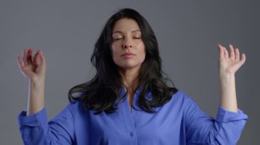Sakin, olgun bir kadın dinleniyor, meditasyon yapıyor. Yetişkin kadın sakinleşiyor, gri stüdyo arka planında derin derin nefes alıyor.