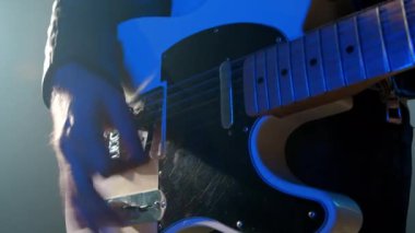 Rock müzisyenlerinin elleri elektro gitar çalarken yakından görülüyor. Sahnedeki konser sırasında dumanlı spot ışıklarıyla tellere dokunan parmaklar
