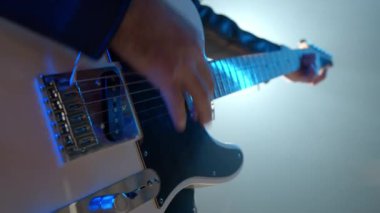Rock müzisyenlerinin elleri elektro gitar çalarken yakından görülüyor. Sahnedeki konser sırasında dumanlı spot ışıklarıyla tellere dokunan parmaklar