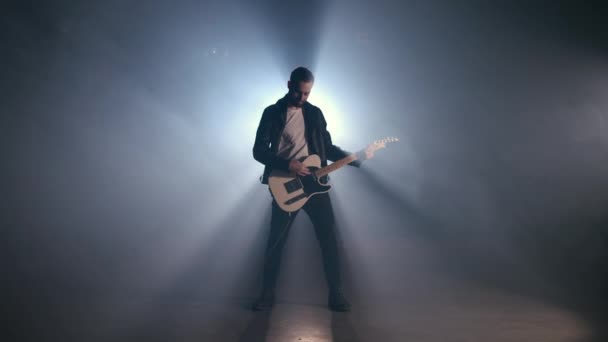 Rockový kytarista na kouřovém pódiu a mistrovsky hrající na elektrickou kytaru. Pohled hudebníka zvedá ruku na konci jako gesto a symbol úspěchu, svobody a vítězství — Stock video