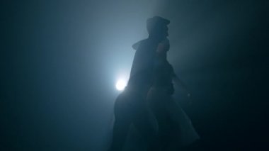 Zarif balerin ve erkek partneri karanlıkta klasik ya da modern bale öğeleri ile sahne ışıkları altında dans ediyorlar. Siyah arka planda sigara içen bir çift. Sanat konsepti. 