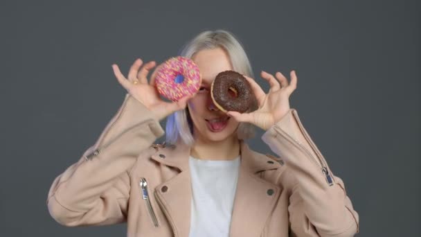 Portrait of cheerful beautiful hipster woman dancing with sweets colorful donuts isolated on grey studio background. Concept of joy, happiness, lifestyle. — Stock Video