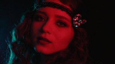 Great Gatsby tarzı giyinmiş eski moda kadın. Karanlık arka planda neon ışıkla poz veriyor. Kükreyen yirmiler, retro, parti, moda konsepti